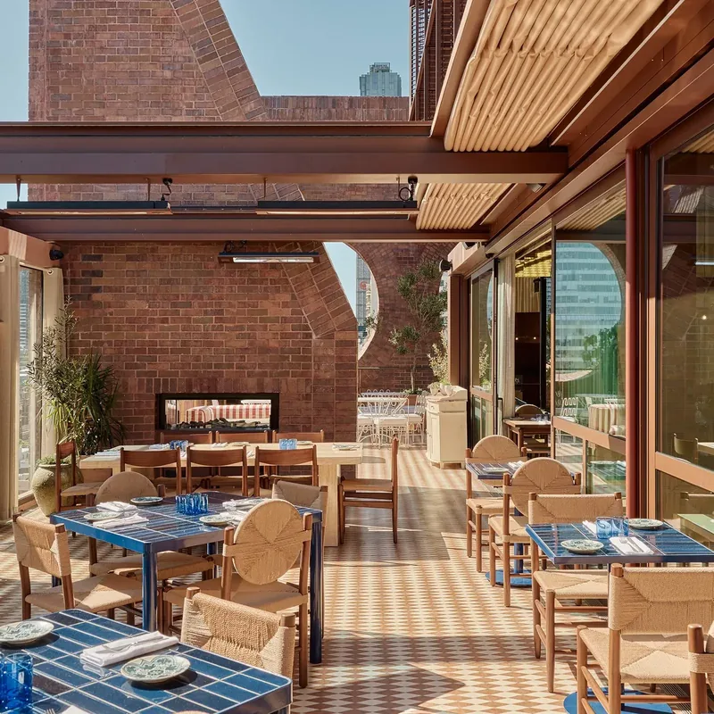 Rooftop terrace at Cleo with blue tiled tables, woven chairs and a brick fireplace