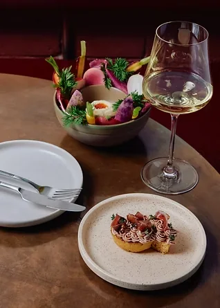 Tasting menu course and glass of white wine on a dark timber table at Amaru