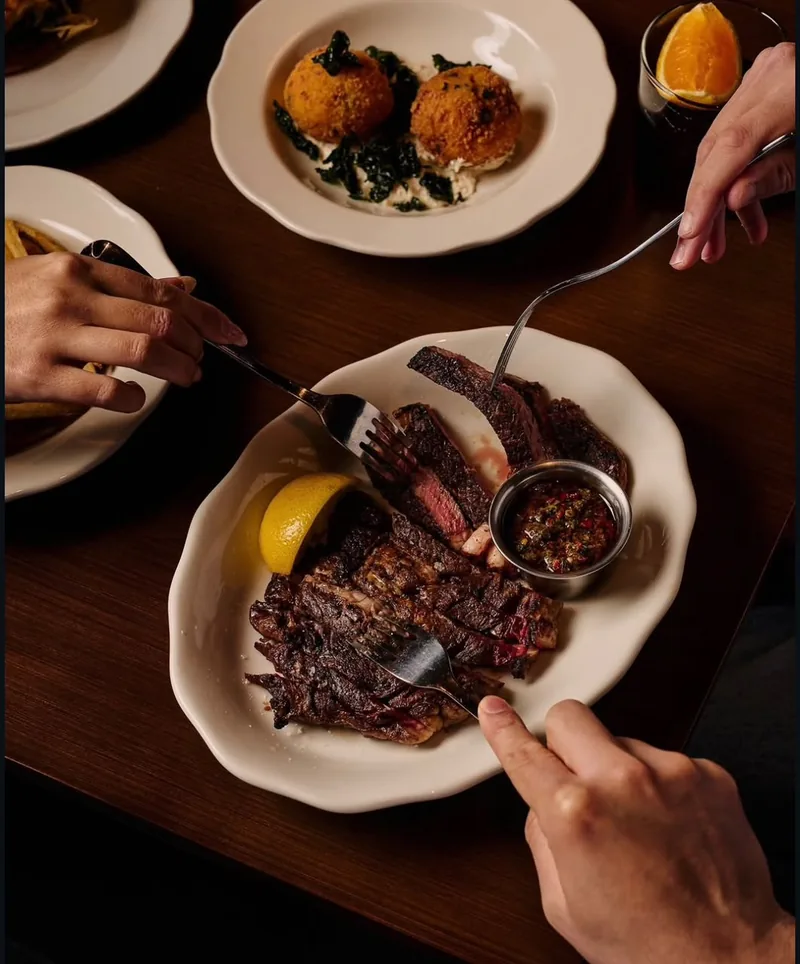 Sliced steak with chimichurri, croquettes and fries shared across a dark timber table