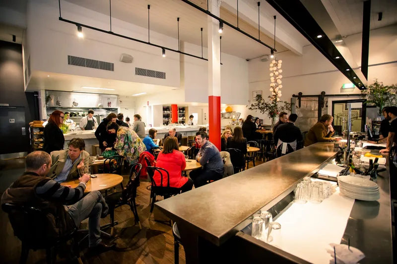 Diners at tables and the long steel bar in the evening at Cumulus Inc.